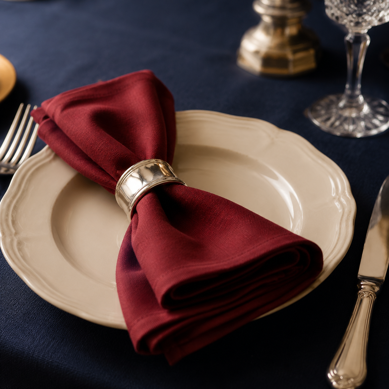 Close detail of a place setting with ivory plate, silver cutlery and a burgundy napkin