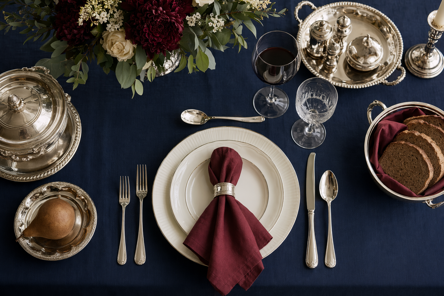 Formal table setting on ink navy linen with ivory plates and polished silver-tone serveware